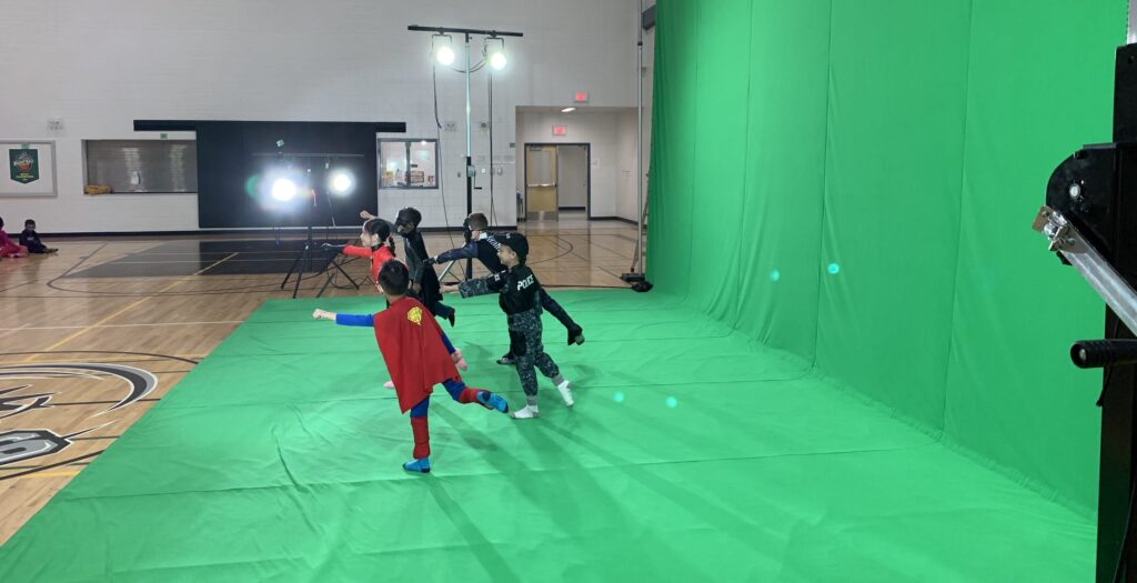 Green screen in a school gyn with five children in costumes pointing