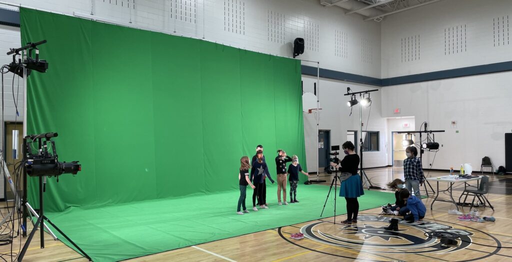 huge green screen set up in school gym with children in costumes acting for a camera
