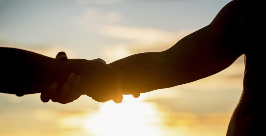 a silhouette of two people hold hands with the sun in the background