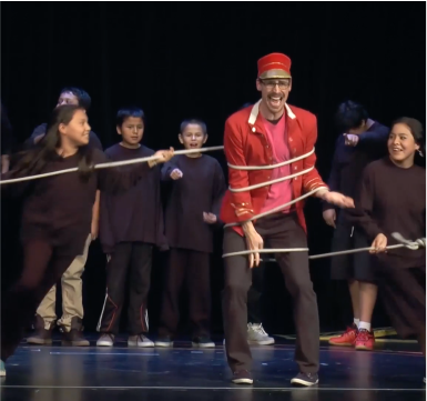 man wearing a red blazer with red hat is tied with rope by a group of students wearing all black