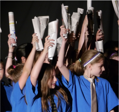 children in blue shirts hold newspapers up in the air