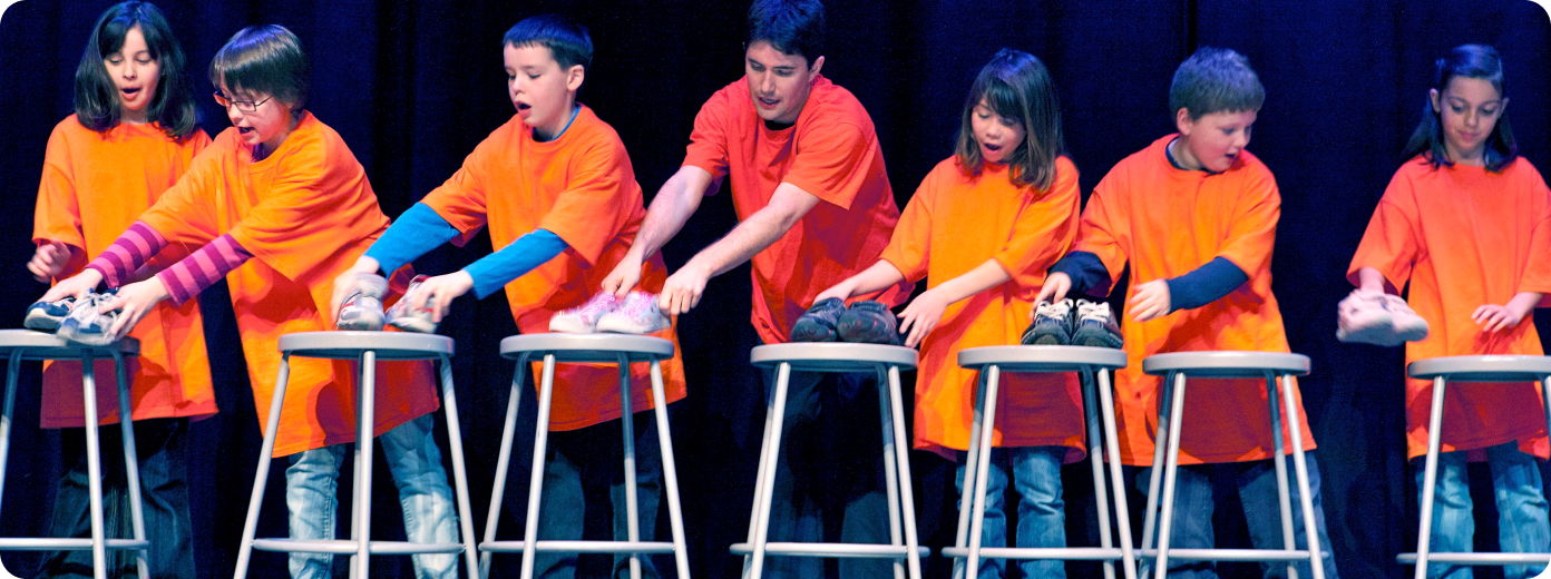 children wear orange shirts and reach out for shoes