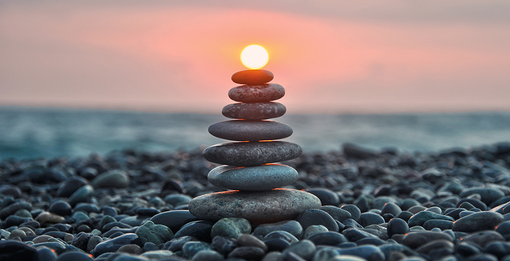 Formation of rocks piled up on each-other with the sun in the distance on a rocky beach