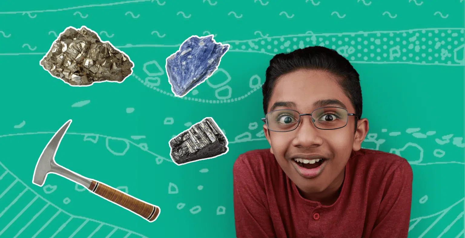 little boy wearing glasses in maroon top smiles at camera with hammer and minerals floating in the background