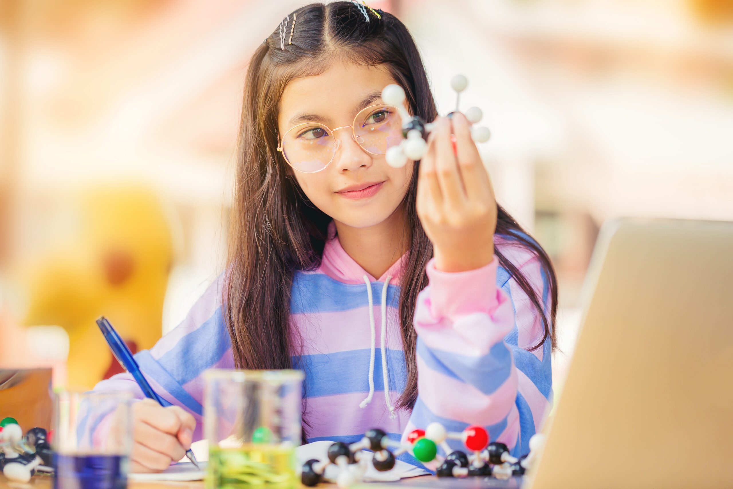 Asian teenage girl in elementary science class doing chemical model form and taking notes.